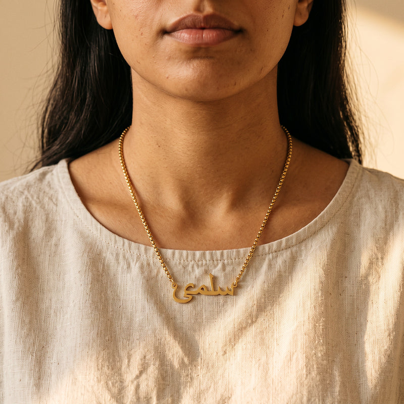 Gold Arabic name necklace on box chain worn with a linen top