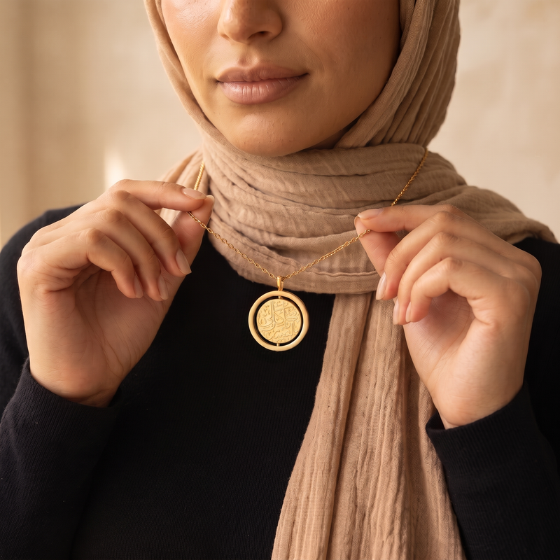 Close-up of the gold Noor spinning pendant held between the fingers