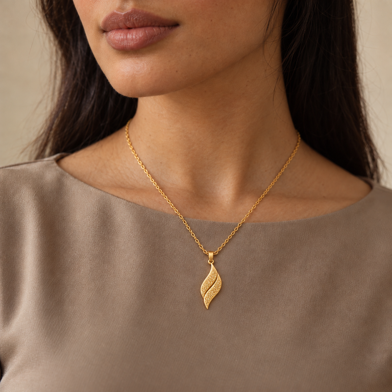 Woman wearing the gold calligraphy leaf necklace with a taupe top