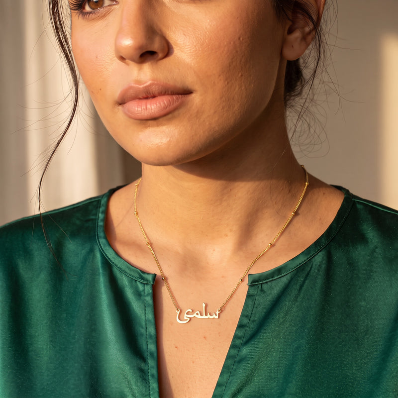 Gold Arabic name necklace on satellite chain worn with an emerald satin top